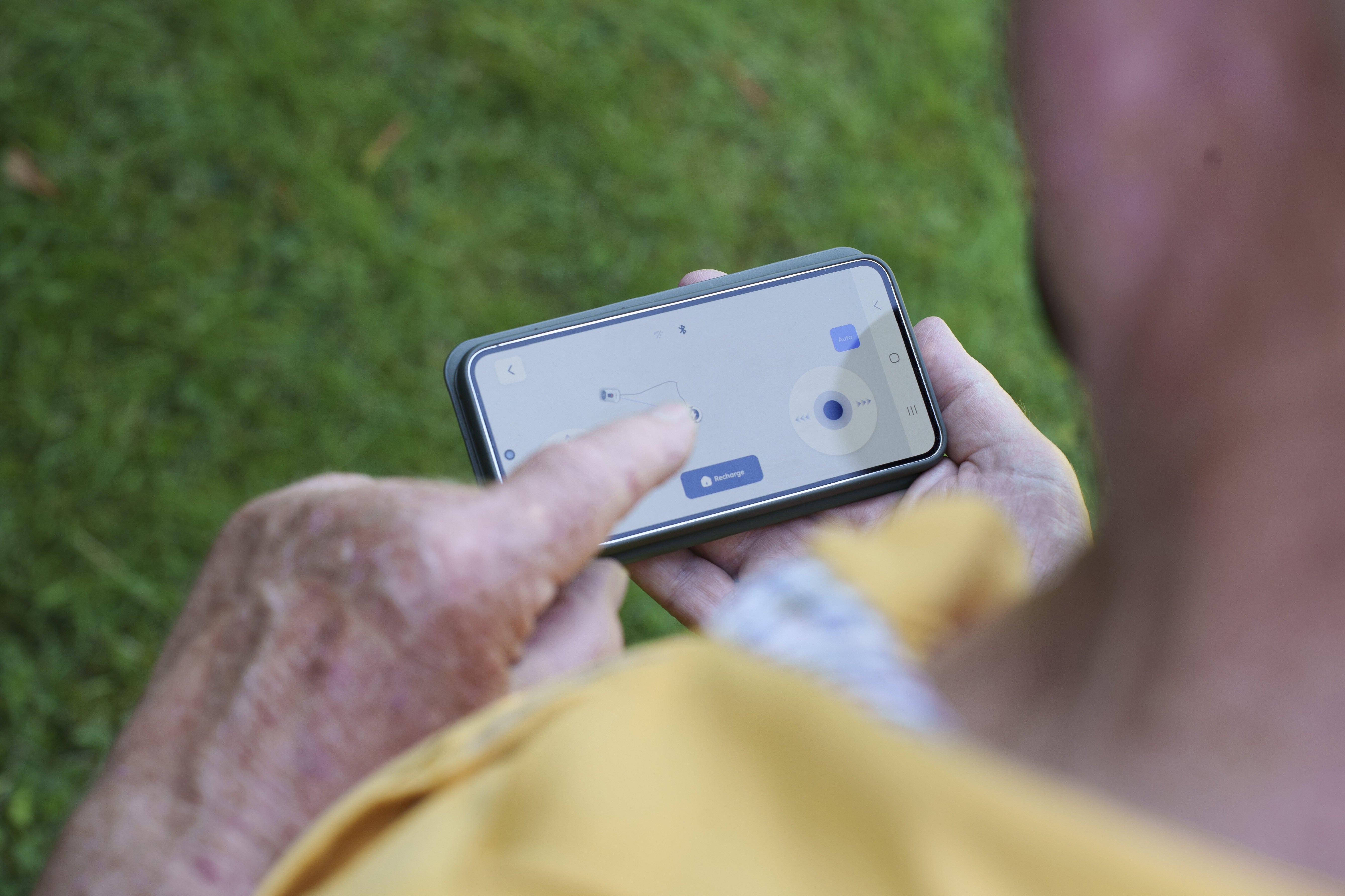 Senior man using smartphone to control ANTHBOT wireless robotic lawn mower app.